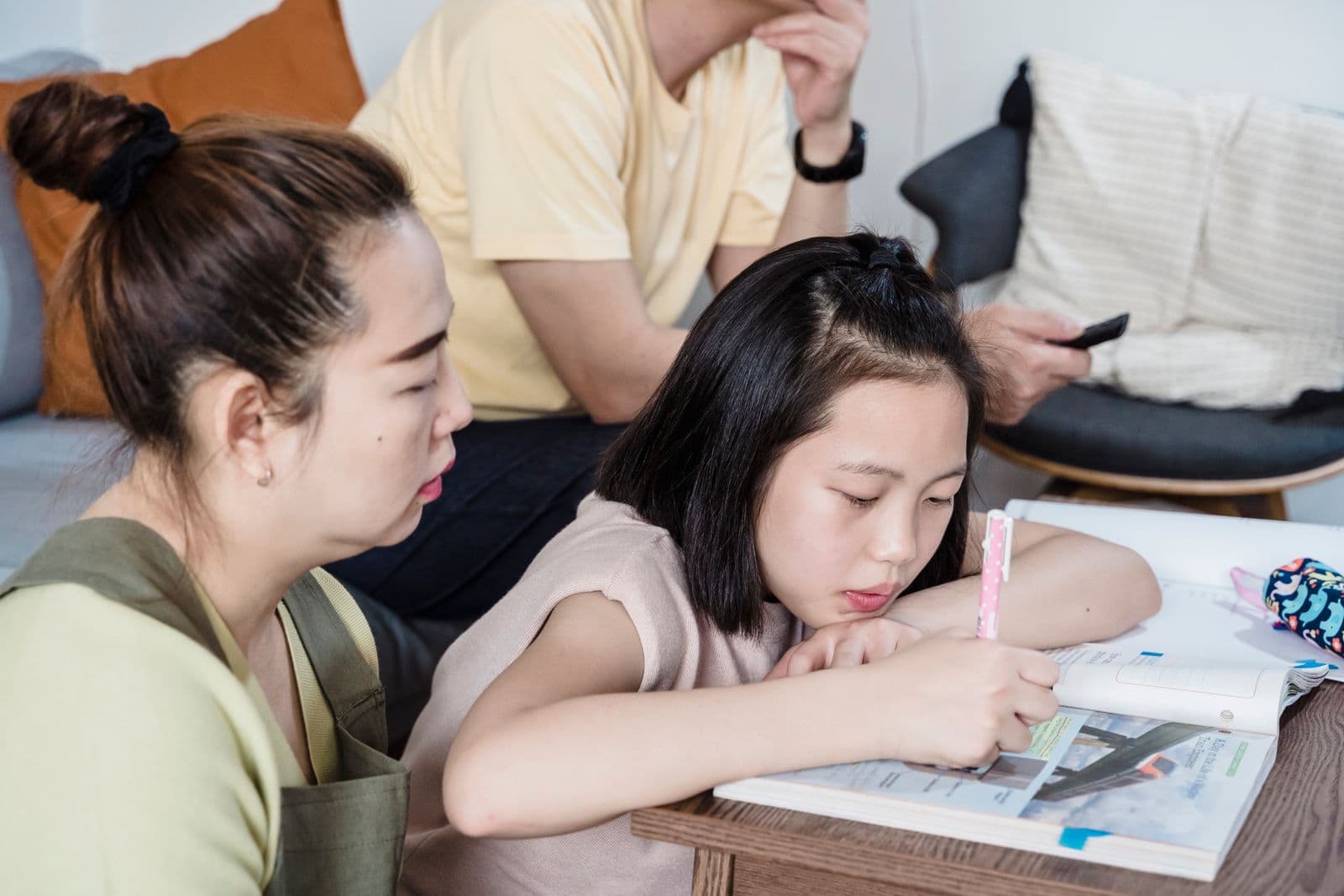 A parent sitting beside their primary-school child, helping with homework at the kitchen table.