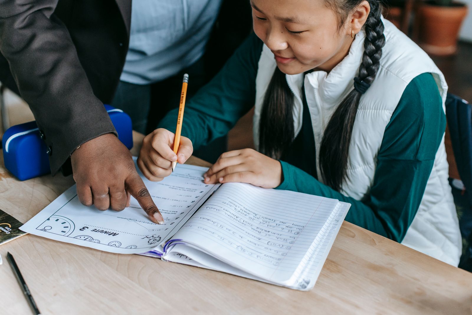 An educator guiding a focused, smiling child through a workbook at a desk.
